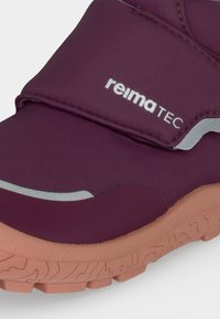 Κοντινή λήψη ενός παπουτσιού Reima Tec σε μπορντό χρώμα με ανακλαστικές λεπτομέρειες και υφασμένο ανοιχτό καφέ λαστιχένιο πάτο.