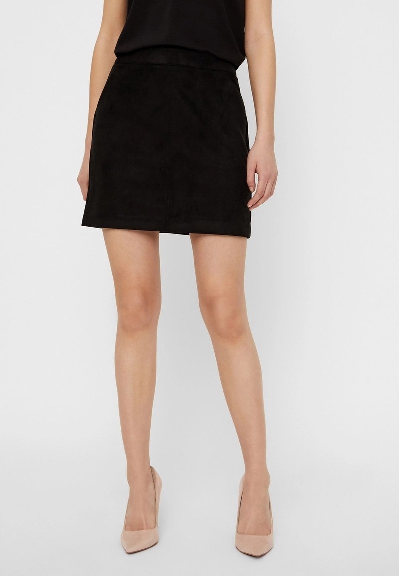 Svart mocka minikjol med en slät textur och en åtsittande design, med en midjehöjd i mellanläge och en subtil fåll. Kombinerad med beige klackar.