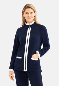 Marineblaue Sweatjacke mit Reißverschluss und weißer Kante, ausgestattet mit hohem Kragen, zwei Vordertaschen und weicher Textur. Akzentuiert mit vertikalen weißen Streifen.