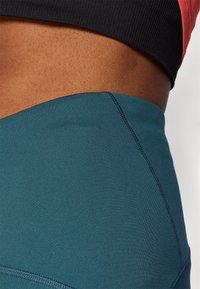 Høytlivte turkise treningstights med en jevn tekstur og flate sømmer. Capri-lengde med en konturert design.