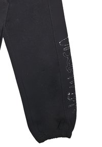 Pantaloni neri con una vestibilità affusolata, caratterizzati da una morbida texture e polsini elasticizzati. Dei brillanti decorativi in argento formano un design lungo il lato.