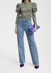 Blusa a maniche puff con motivo floreale e texture; jeans azzurri a vita alta e gamba dritta; pochette viola; tacchi a spillo viola.