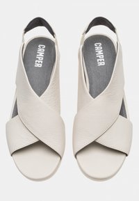 Sandali in pelle grigia chiara con fasce incrociate, tacco aperto e suola piatta. Presentano il logo "Camper" in rilievo sulla soletta grigia.