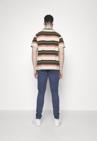 Koszulka w paski w kolorach beżowym, zielonym, czerwonym i czarnym; niebieskie spodnie; białe trampki. Koszulka ma krótkie rękawy i okrągły dekolt.