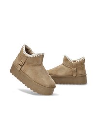 Botas de tobillo de ante color arena con un acabado texturizado, forro de felpa y un borde con zigzag en el cuello. Presenta un detalle de hebilla lateral y una suela de plataforma gruesa.