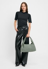 Czarna bluzka z krótkim rękawem, błyszczące skórzane spodnie z wysokim stanem oraz dużą zieloną skórzaną torbą z zakrzywionym uchwytem.