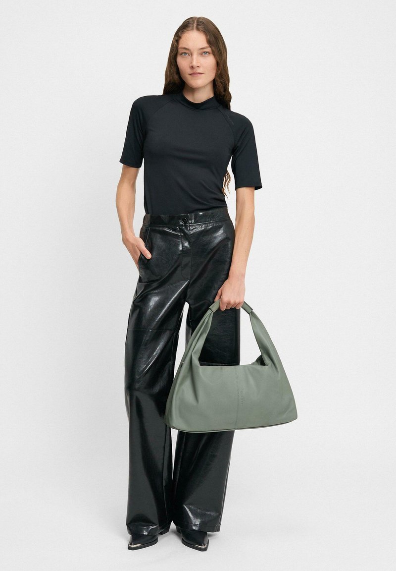 Czarna bluzka z krótkim rękawem, błyszczące skórzane spodnie z wysokim stanem oraz dużą zieloną skórzaną torbą z zakrzywionym uchwytem.