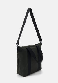Grønn vanntett tote bag med svarte stropper. Rektangulær form, med robuste håndtak og justerbar skulderreim. Enkel design.
