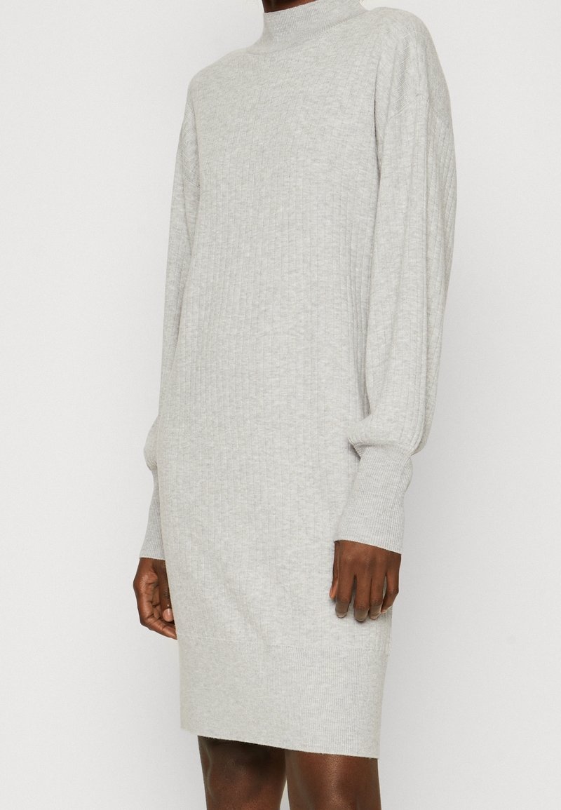 Robe-pull en maille côtelée gris clair avec manches longues ballon et col montant, portée par une personne devant un fond uni.