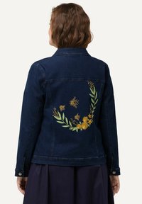 Chaqueta de mezclilla azul oscuro con bordados de flores y abeja en la parte trasera, con hojas verdes, flores amarillas y detalles texturizados.