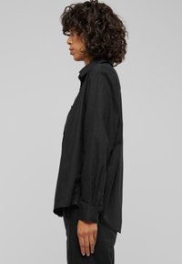 Black button-up shirt in lightweight fabric, featuring a pointed collar, long sleeves, and a straight cut with side slits.