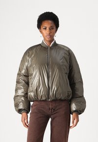Olivgrüne Steppjacke mit hohem Kragen, Reißverschluss vorne und gerippten Bündchen. Verfügt über eine glänzende Oberfläche und eine voluminöse, gesteppte Form.