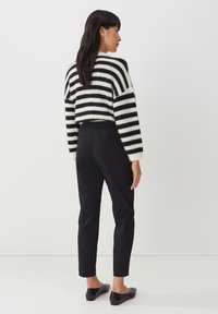 Zwart-wit gestreepte, cropped pullover trui in combinatie met nauwsluitende zwarte broeken, voorzien van een subtiele achterzak. Glad, strak materiaal.