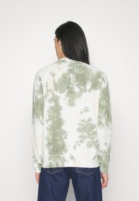 Sudadera de tie-dye verde y crema con cuello redondo, mangas largas y puños y dobladillo acanalados. Textura suave, corte informal y sin logotipos visibles.