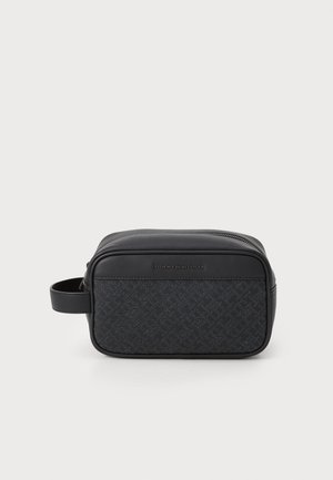 Black toiletry bag with a textured front panel and smooth sides. Features a zip closure and a side handle. Subtle brand logo on the front.