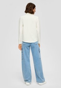 Lange mouw crème top met een afgeronde zoom, gecombineerd met lichtblauwe cargo-broek met wijde pijpen, voorzien van zijzakken en een relaxte pasvorm.