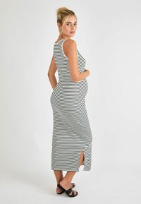 Vestido de maternidad sin mangas a rayas en blanco y negro, diseño ajustado con abertura lateral, hecho de tela suave y elástica. Sandalias negras.