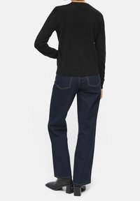 Schwarzer Strickpullover mit Rundhalsausschnitt, kombiniert mit dunkelblauen geraden Jeans mit kontrastierenden Nähten und schwarzen Stiefeletten mit Absatz.