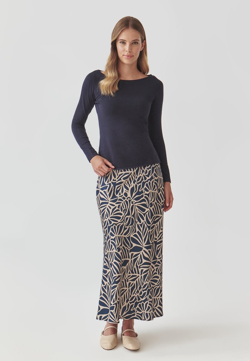 Granatowa bluzka z długim rękawem połączona z beżową spódnicą do ziemi z granatowym wzorem liści, uzupełniona jasnymi butami.