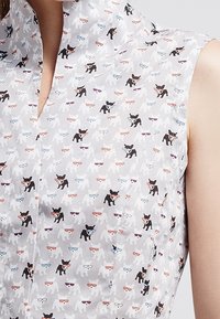 Hihaton paita, jossa on pieniä mustia ja valkoisia koiria värikkäissä laseissa kevyellä taustalla.