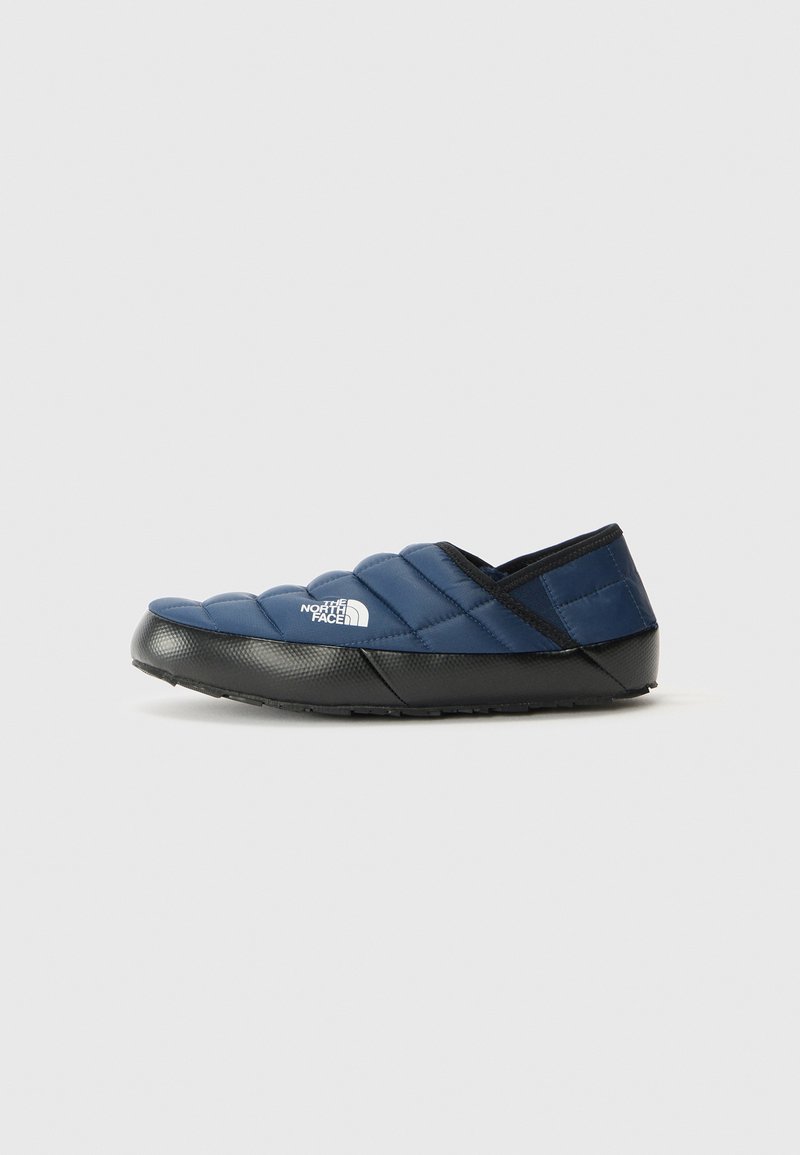 Chinelo slip-on acolchoado azul marinho com sola preta e o logotipo da The North Face de lado, posicionado à direita sobre um fundo simples.