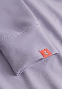 Lichtpaarse sweatshirt met een gemêleerd oppervlak. Voorzien van een rood label op de manchetten met een witte graphic. Betrouwbare naden en modern ontwerp.