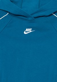 Tawna kokvilnas kapuce ar auklu, kurai ir balts Nike logo un kontrastējoša balta šuvju dūriena.
