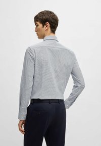 Camicia a maniche lunghe con un motivo geometrico blu e bianco. Collo con bottoni, tessuto testurizzato e dettagli ai polsini. Indossata con pantaloni scuri.