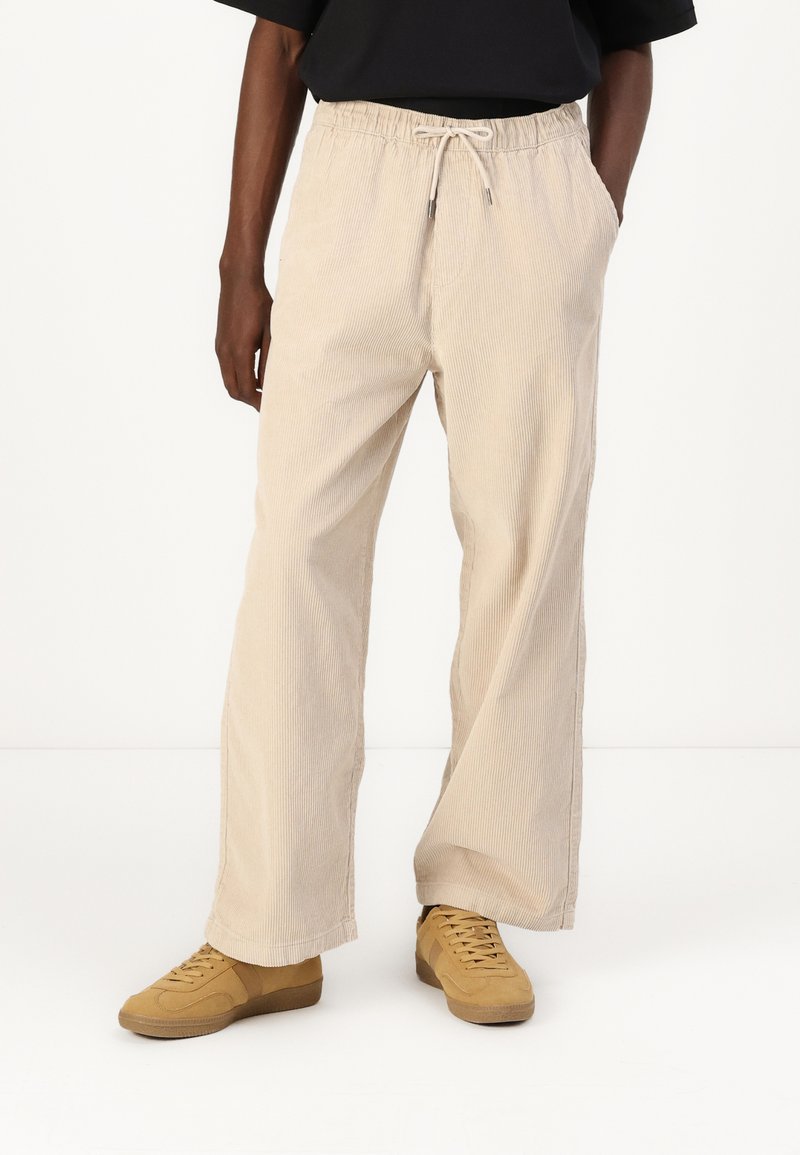 Light beige corduroy pants with a relaxed fit, elastic waistband, and drawstring. Features side pockets and subtle ribbed texture.