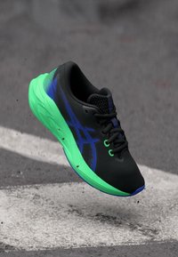 Chaussure de course avec une tige noire, une semelle verte et des accents bleus. Design léger avec des détails texturés pour la respirabilité et le soutien.