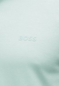 Tissu bleu clair avec logo "BOSS" en relief centré, montrant une texture subtile et des plis sur le matériau lisse.