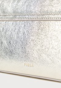 Metalická strieborná kožená kabelka s textúrou, s horizontálnym zipsom a malým zlatým logom "FURLA" pri dolnom okraji.