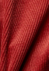 Punainen corduroy-kangas, jossa on kohotettu, pystysuuntainen uritettu pinta. Materiaali vaikuttaa pehmeältä ja ylelliseltä, ja siinä on rikas, syvä sävy.