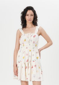 Witte zomerkleed met elastische tailleband en gelaagde rok, voorzien van kleurrijke fruit- en schelpdetails. Brede bandjes en zachte textuur.
