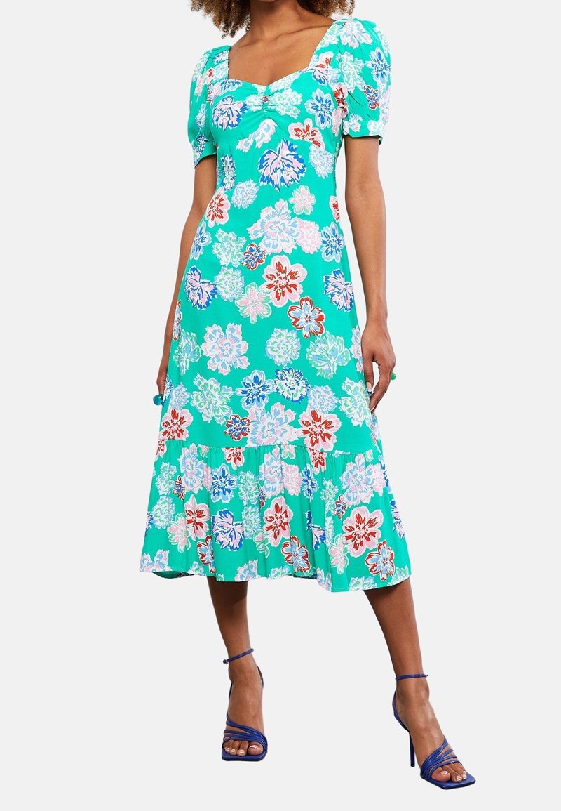 Robe à imprimé floral en turquoise, dotée de manches bouffantes, d'un décolleté carré et d'un ourlet à volants superposés. Agrémentée de fleurs rouges et blanches.