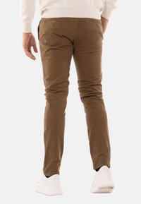 Chinos in cotone marrone con una vestibilità slim, dotati di due tasche posteriori e una superficie liscia, abbinati a sneakers bianche.