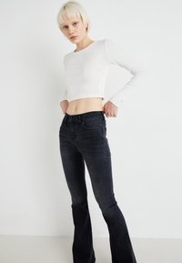 White long-sleeve crop top paired with dark gray flared jeans, featuring front pockets and a smooth texture against a plain background.
