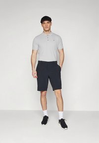 Lysegrå polo-skjorte med to knapper, marineblå shorts, svart caps og svarte treningssko med hvit såle, stående på en ensfarget bakgrunn.