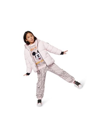 Giacca imbottita rosa, felpa con motivo e grafica di Topolino, e pantaloni stampati in bianco e nero, abbinati a scarpe sportive.