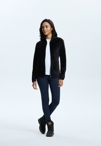Giacca in pile nera, con texture, colletto alto, chiusura con zip e maniche lunghe, abbinata a leggings blu navy e stivali invernali neri.