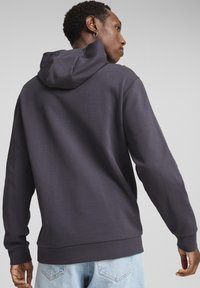 Sudadera gris con un acabado texturizado, capucha y mangas largas. El dobladillo inferior es recto y ajustado; se lleva con jeans de color azul claro.