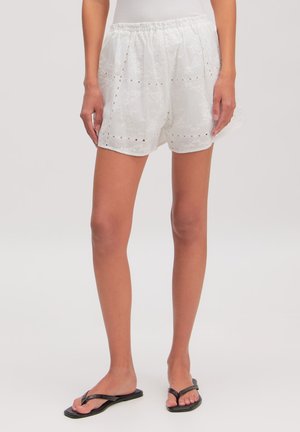 White eyelet lace shorts with elastic waist worn by a person standing, paired with black flip-flop sandals.