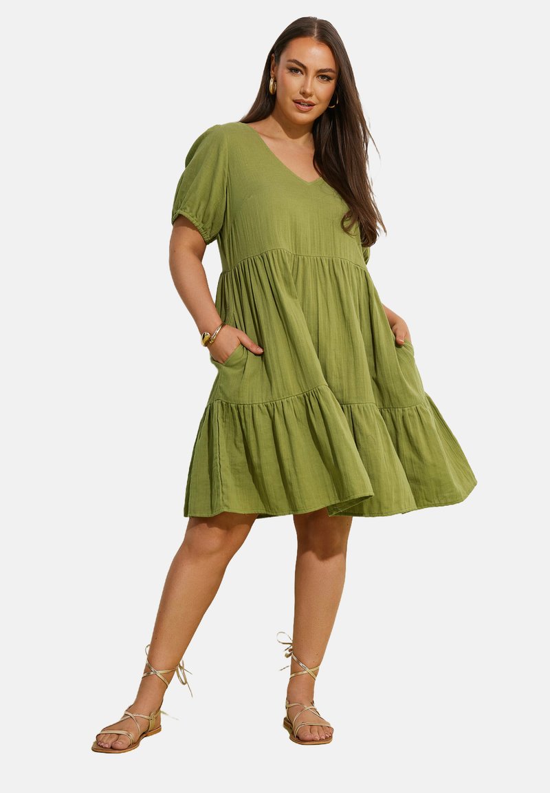 Grünes kurzärmliges, gestuftes Kleid aus leichtem Stoff, mit V-Ausschnitt, Seiten Taschen und lockerer Passform.