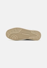Sneaker bianco con una suola in gomma beige testurizzata. Presenta un logo e un battistrada strutturato per una migliore aderenza. Design minimalista con linee morbide.
