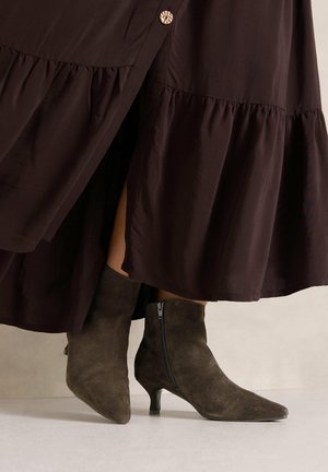 Bottines en daim marron à bouts pointus et talons petits kitten portées avec une jupe marron foncé avec un bouton et un ourlet froncé.