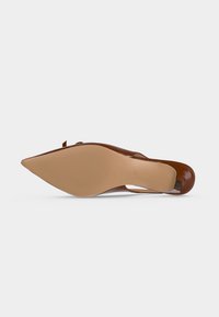 Chaussure à talons hauts marron à bout pointu vue de la semelle, montrant un dessous beige lisse avec une zone de prise circulaire texturée.