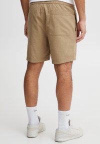 Kaki korte broek met een gestructureerde afwerking, elastische tailleband en een achterzak. Draagt witte sokken en lichte sneakers.