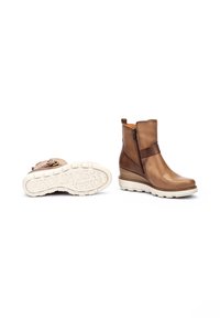Bottes de cheville en cuir marron avec une fermeture éclair sur le côté, dessus texturé et semelle en caoutchouc blanche contrastante, présentant un design à talon compensé pour plus de hauteur.