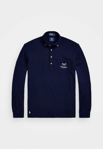 Μπλέ μακρυμάνικο πουκάμισο πόλο φτιαγμένο από βαμβάκι. Διαθέτει γιακά με κουμπιά, τσέπη με κέντημα "Wimbledon" και μικρό λογότυπο στο στρίφωμα.