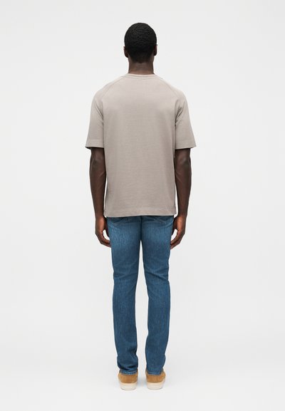 Grey cotton t-shirt with short sleeves, relaxed fit, and raglan seams, paired with blue denim jeans and light tan shoes.